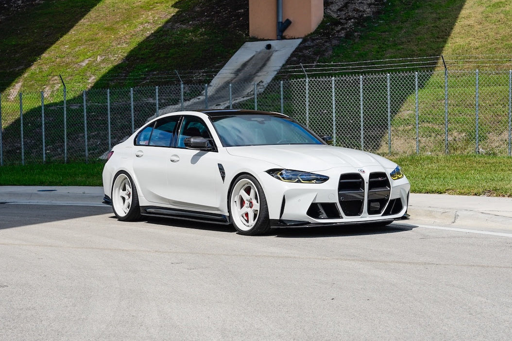 White BMW car on a road with a grassy hill and overpass in the background